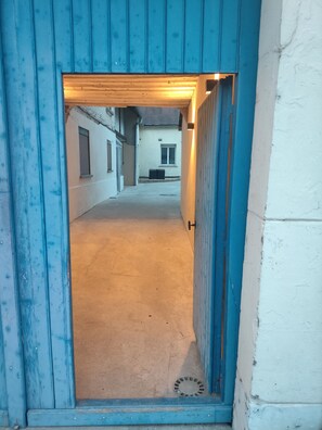 Un pasillo estrecho con una puerta azul que da a una habitación con ventana y puerta.