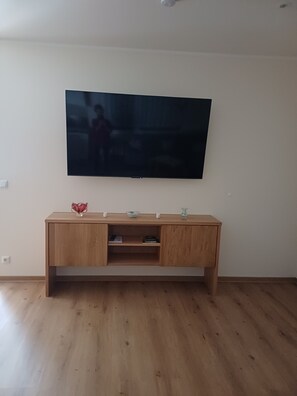 A living room with a flat-screen TV mounted on the wall, a wooden console table with decorative items, and a wooden floor.