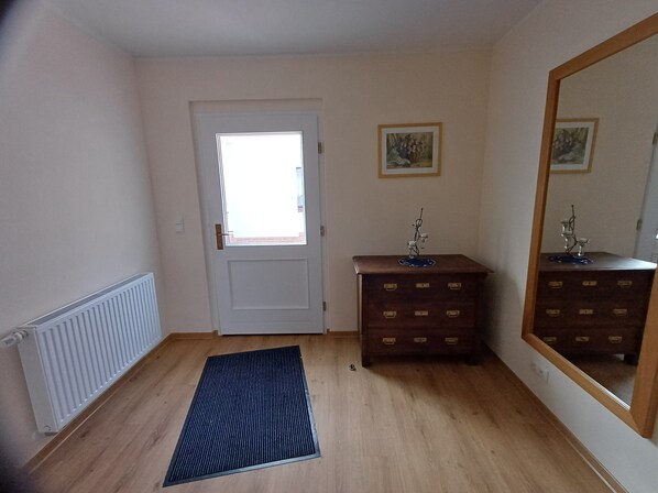 A room with a radiator, a door with a window, a dresser with drawers, and a mirror on the wall.