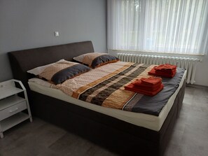 A neatly made bed with a patterned bedspread, pillows, and folded red towels.