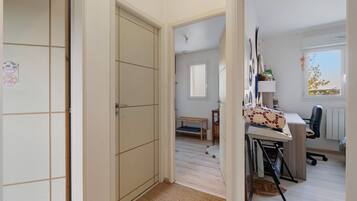 Un couloir menant à une pièce où se trouvent un bureau, une chaise et une fenêtre donnant sur un paysage.