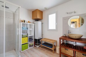 Un bany amb dutxa, vàter, un lavabo amb rentapousa, mirall i prestatges amb productes de tocador.