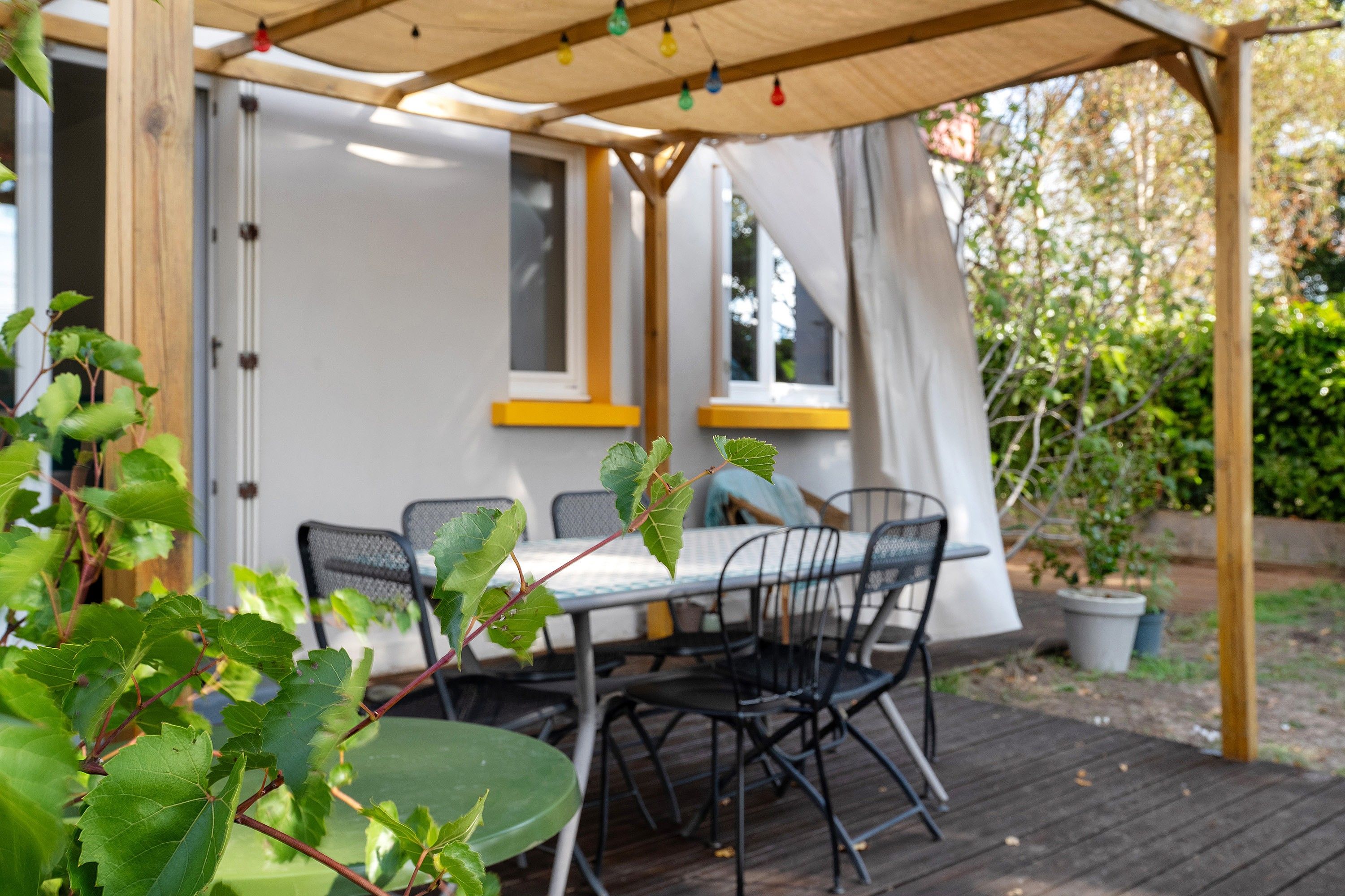 Une terrasse extérieure avec une table et des chaises, entourée de verdure.