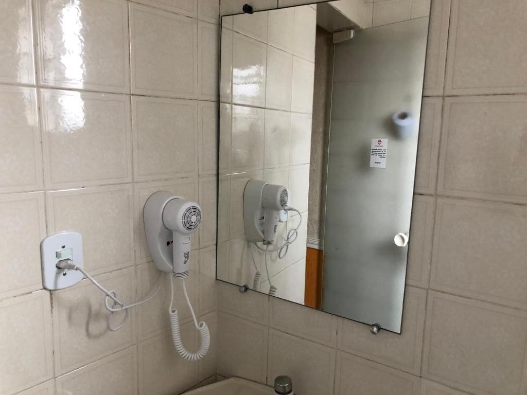Ein Badezimmer mit Fön, der an der Wand angebracht ist, einem Spiegel und einem Handtuchhalter.