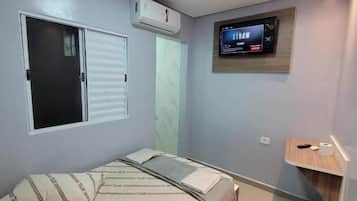 A bedroom with a bed, a TV mounted on the wall, and a window with blinds.