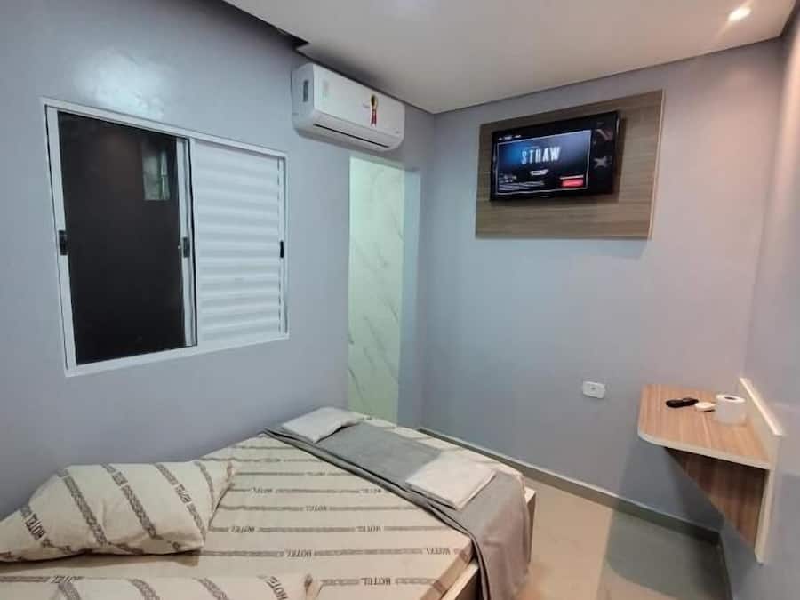 Une chambre à coucher avec un lit, un téléviseur fixé au mur et une fenêtre avec des stores.