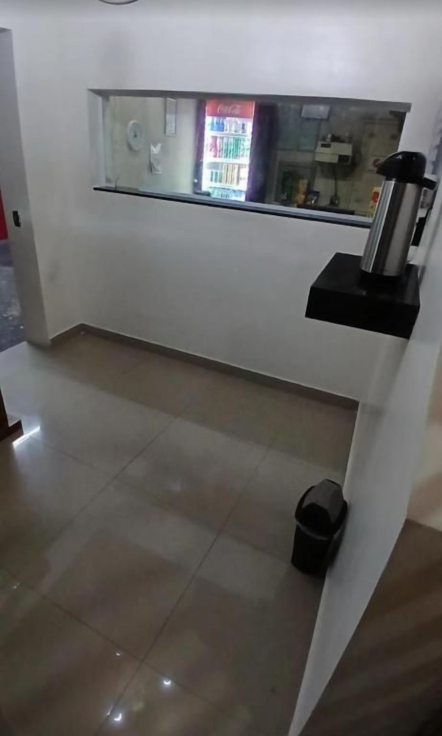 Une pièce avec un sol carrelé, une poubelle noire, une étagère noire avec un distributeur d’eau et une fenêtre avec un distributeur automatique.