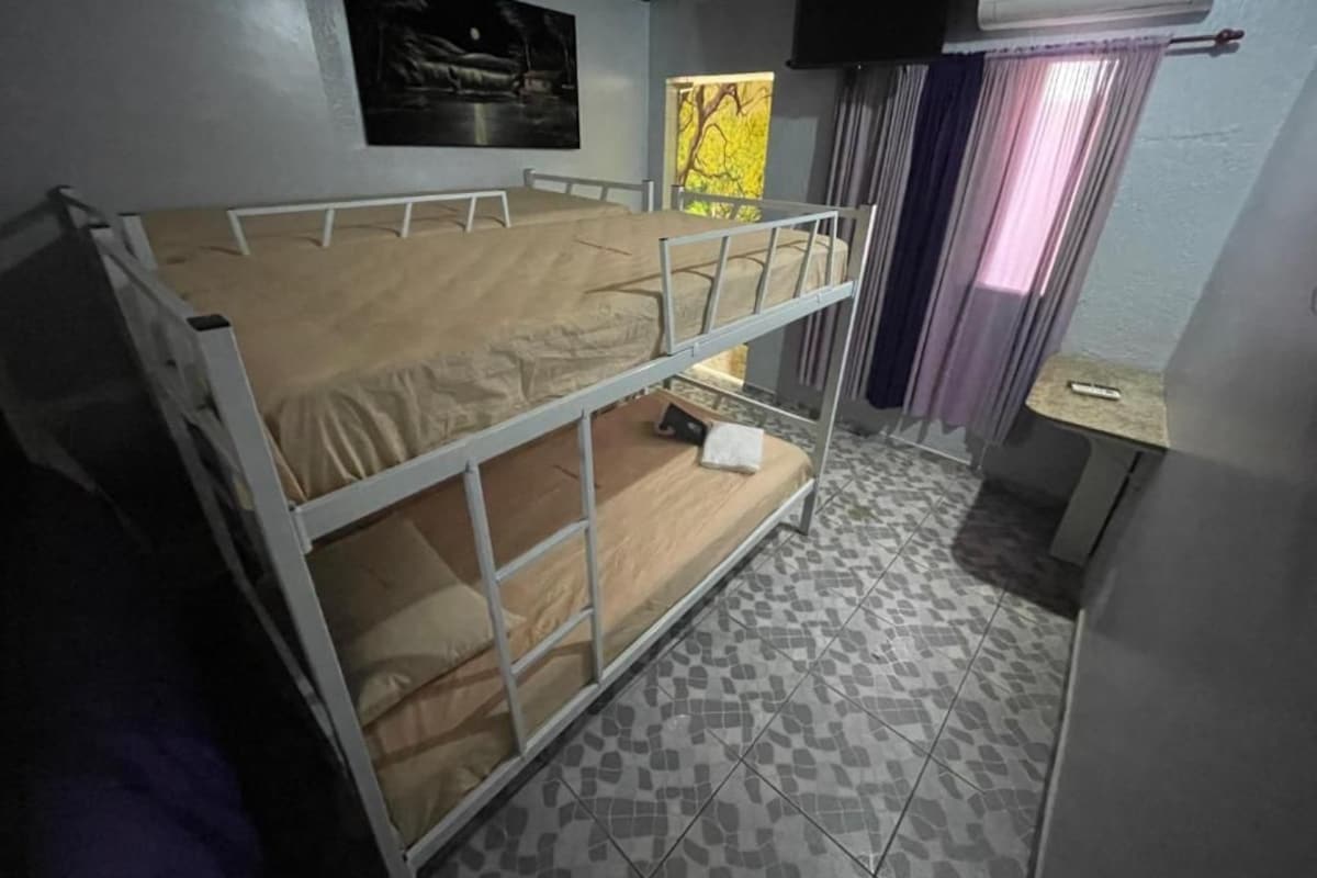 A bunk bed room with a television, a window with curtains, and a tiled floor.