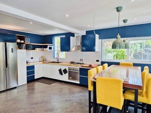 Cocina moderna con comedor, que incluye un refrigerador de acero inoxidable, estufa y un amplio ventanal con vistas a zonas verdes.