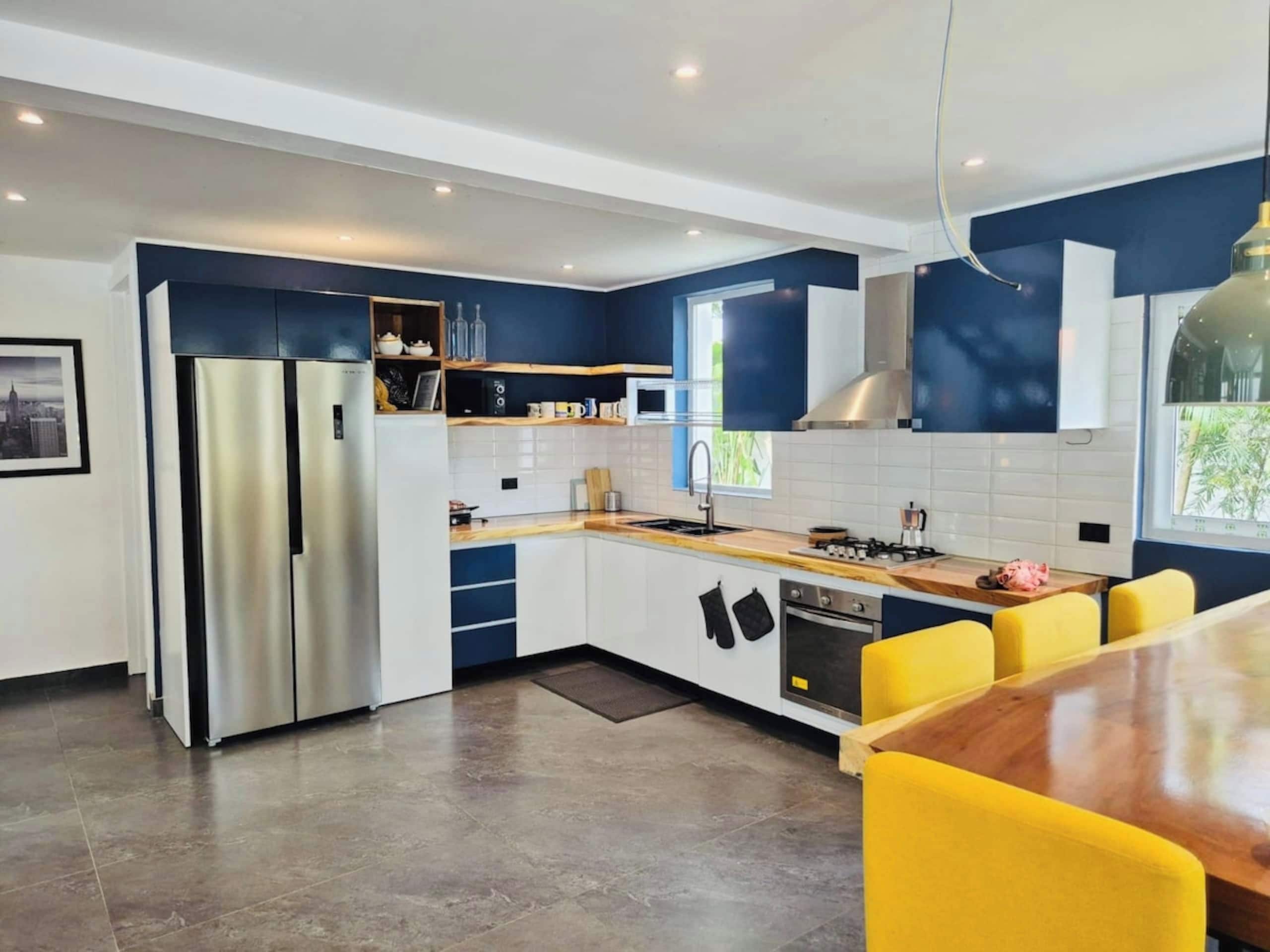 A modern kitchen with a central island, built-in appliances, and a dining area with yellow chairs.
