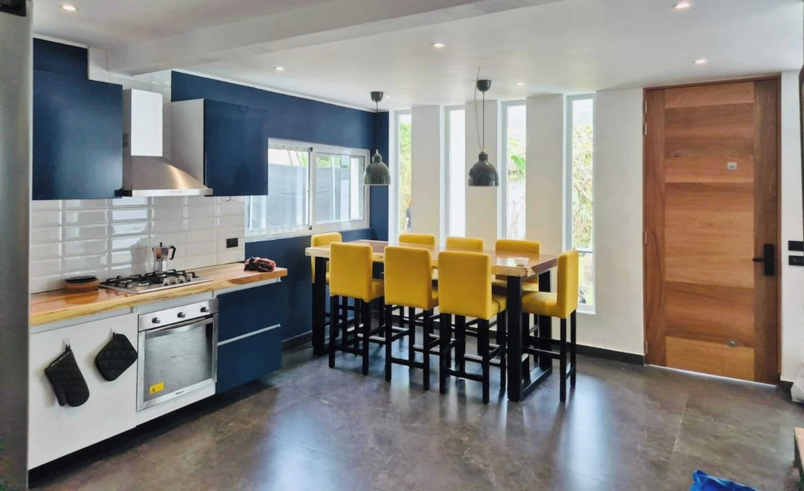 Een moderne keuken met een eethoek, voorzien van een fornuis, oven en gele stoelen.