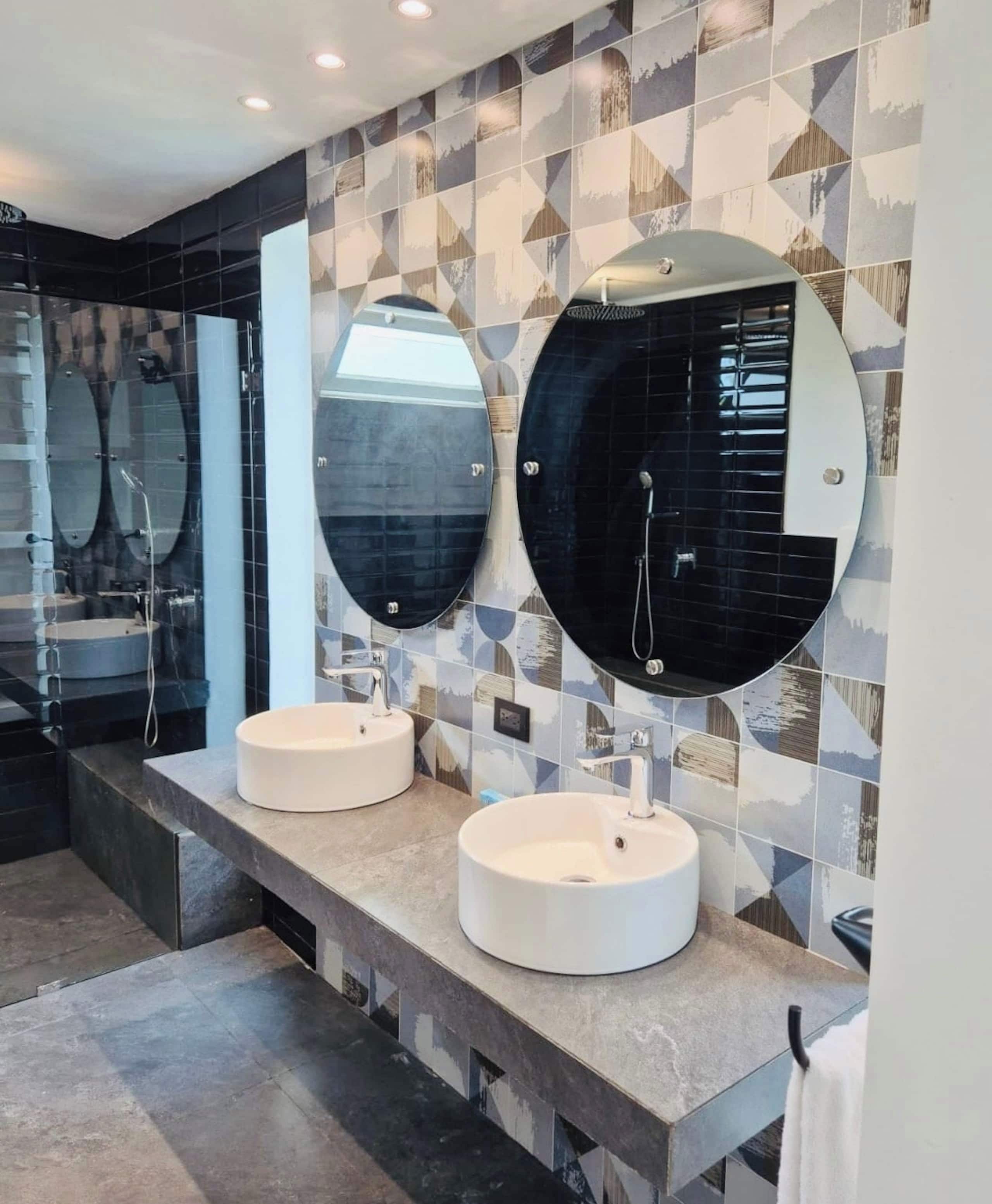 A modern bathroom with two round mirrors, two sinks, and a tiled backsplash.