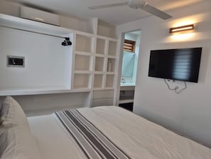 Un dormitorio con cama, televisor montado en la pared, ventilador de techo y estantería empotrada.