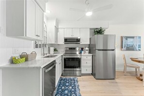 Une cuisine moderne avec des meubles blancs, des appareils en acier inoxydable, un ventilateur de plafond et un tapis à motifs bleus.