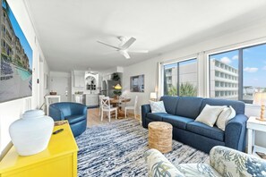 Ein modernes Wohnzimmer mit einem blauen Sofa, einem gelben Beistelltisch und einem großen Fenster mit Blick auf ein Gebäude.
