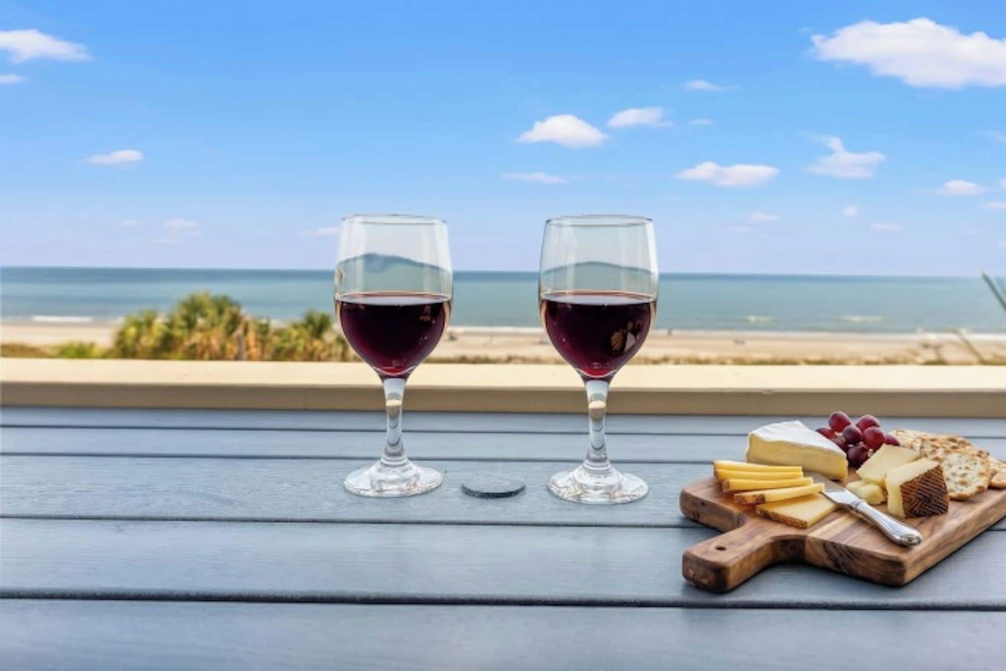 Due bicchieri di vino su un tavolo di legno con vista sulla spiaggia e sull'oceano.