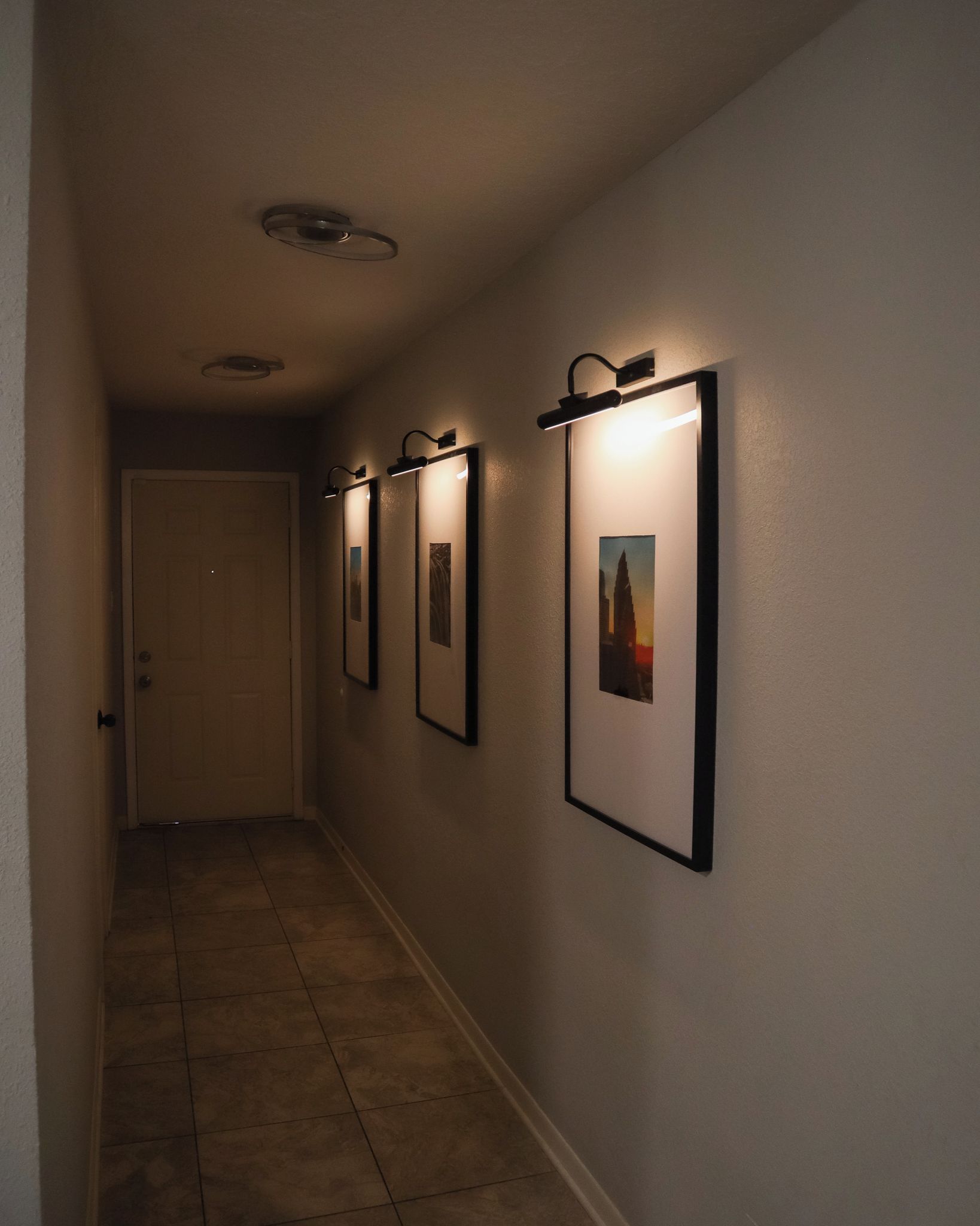 A hallway with framed pictures on the wall and a door at the end.