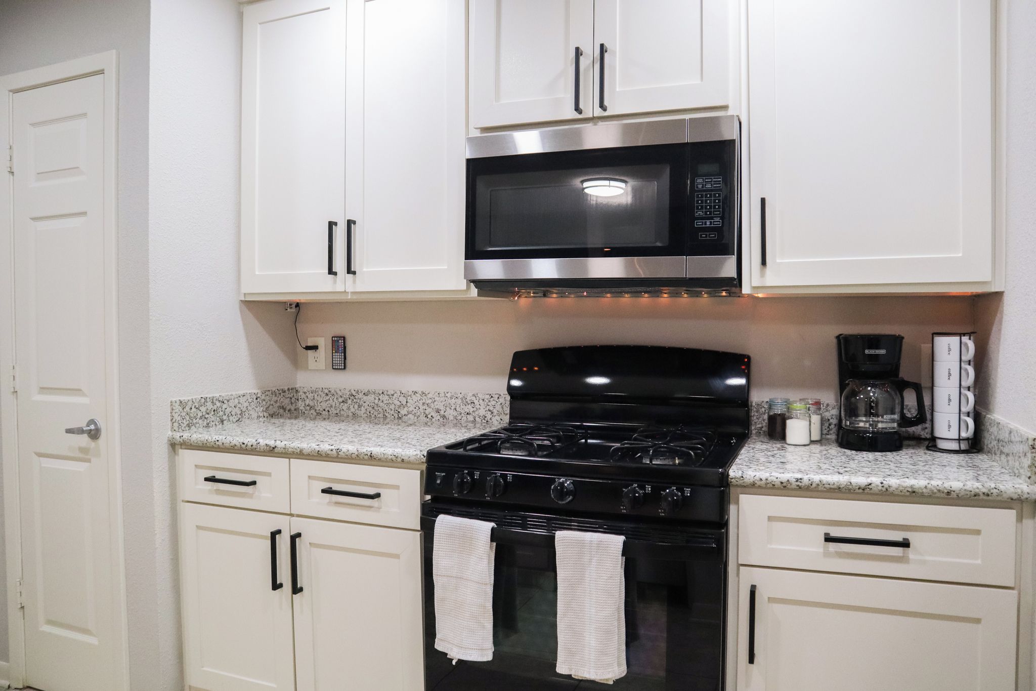 A kitchen with white cabinets, a black stove, a microwave, and a coffee maker.