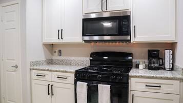 A kitchen with white cabinets, a black stove, a microwave, and a coffee maker.