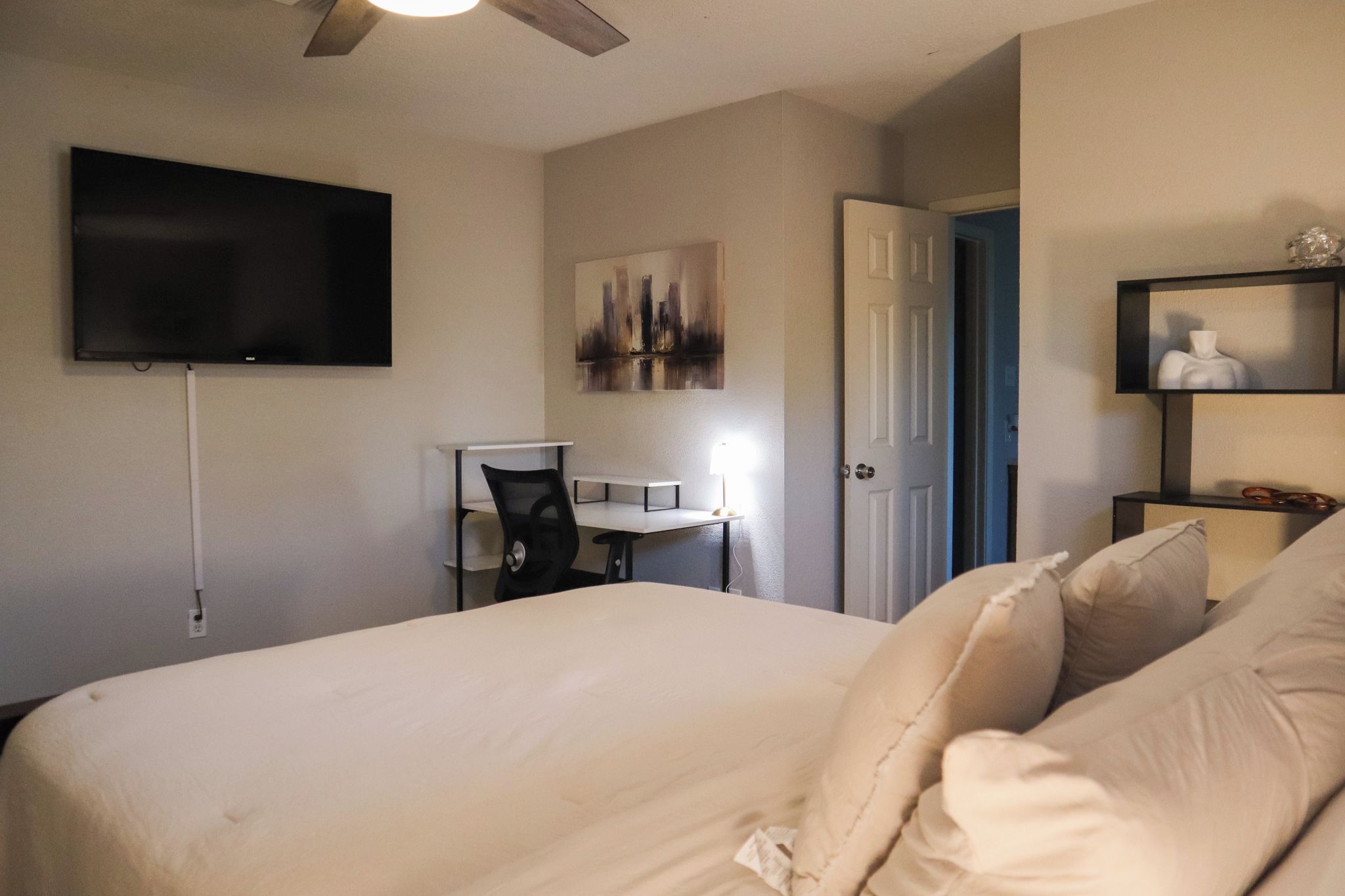 A hotel room with a bed, a desk, a chair, a television, and a door.