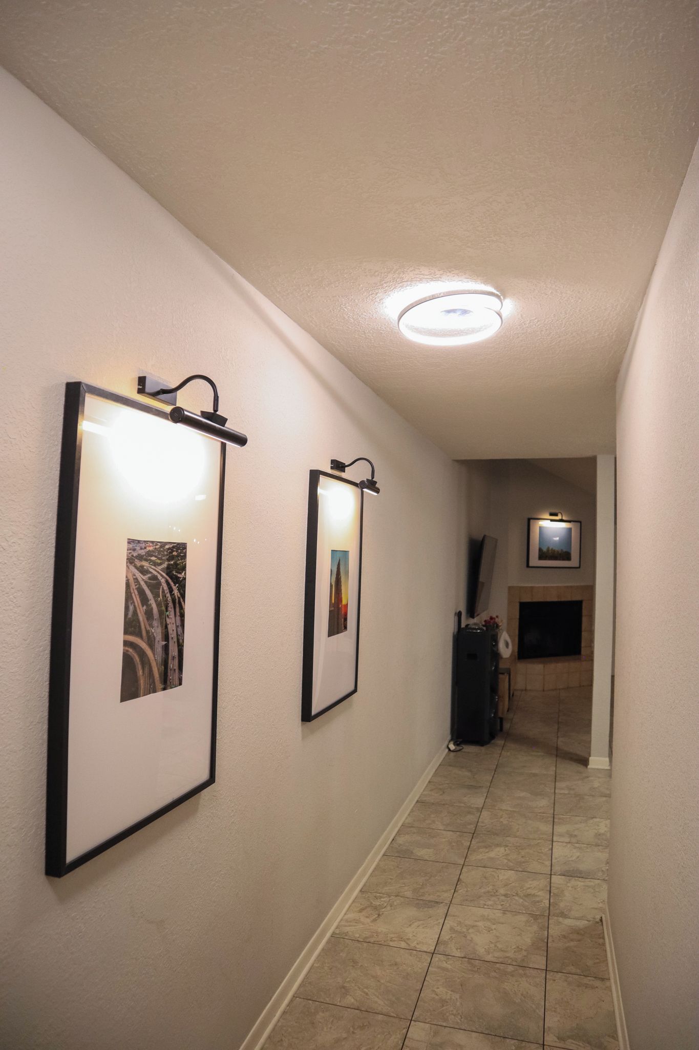 Um corredor com quadros nas paredes, uma luminária no teto e uma lareira ao fundo.