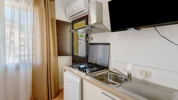 A compact kitchen with a gas stove, a built-in oven, a sink, and a wall-mounted TV.