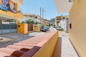 Una calle estrecha con edificios amarillos, una acera con baldosas y coches aparcados.