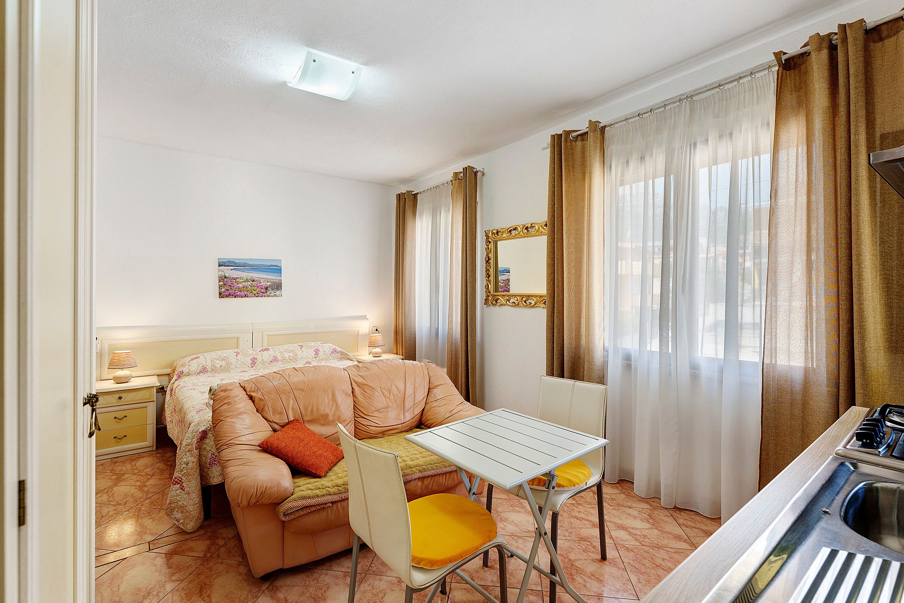Une chambre d’hôtel de taille modeste, comprenant un lit, une petite table, une chaise, un miroir et une fenêtre avec des rideaux.