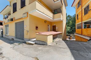 Edificio de dos pisos con puerta de garaje cerrada, un pequeño porche con techo de tejas y el número 12 visible en la pared.