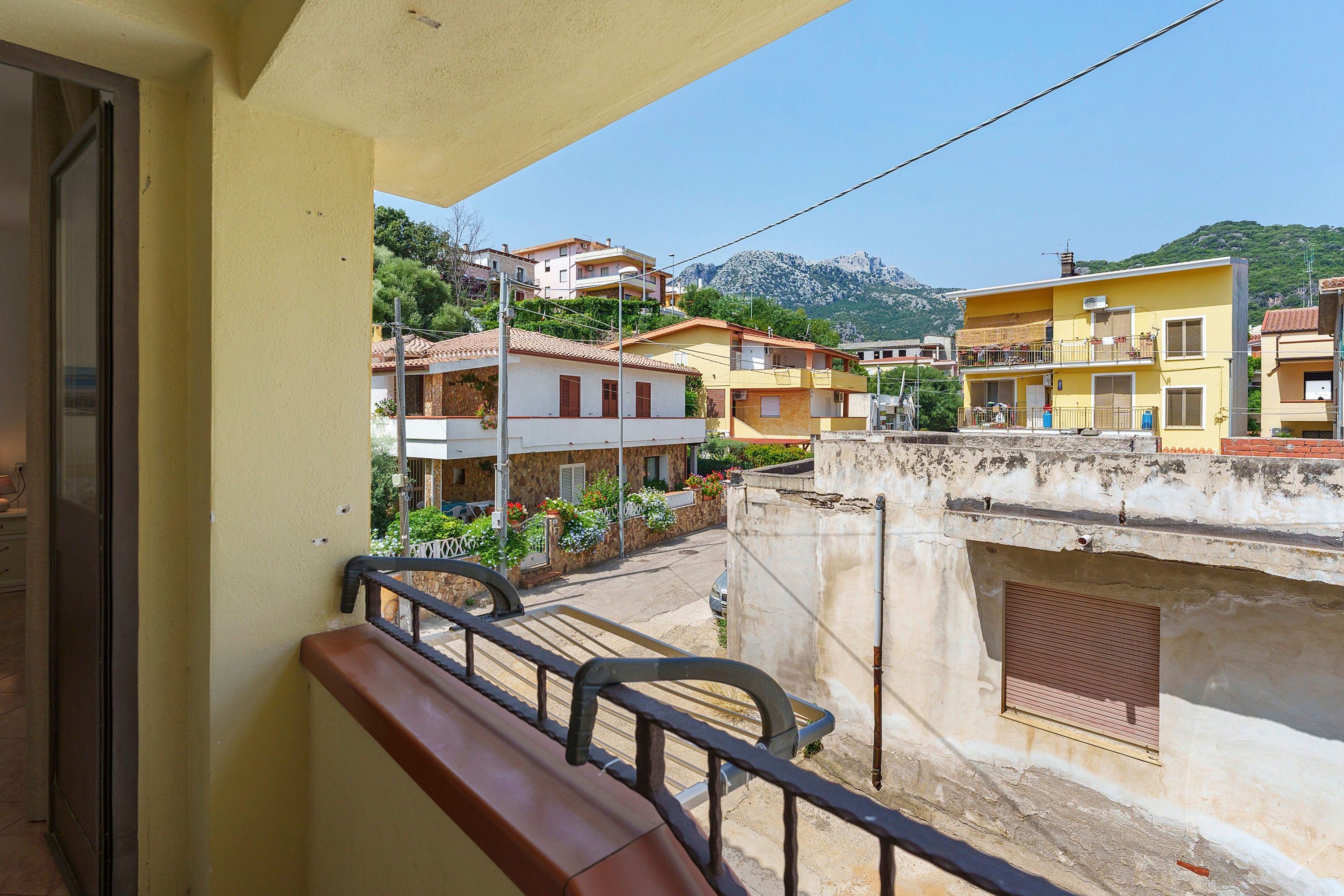 Ein Balkon mit Metallgeländer, Blick auf eine Straße mit Gebäuden und ein Berg im Hintergrund.