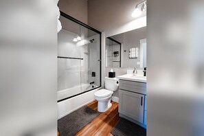 A modern bathroom with a glass-enclosed shower, a white toilet, and a vanity with a mirror. - Hybrid King Bed•Pets Ok•Walkers Paradise•500mbps (Reno)