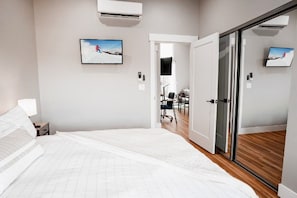 A hotel room with a bed, a desk, and a chair, and a door leading to another room. - Hybrid King Bed•Pets Ok•Walkers Paradise•500mbps (Reno)