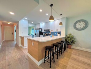 Une cuisine moderne avec un îlot central, des tabourets de bar, des luminaires suspendus et une horloge au mur.