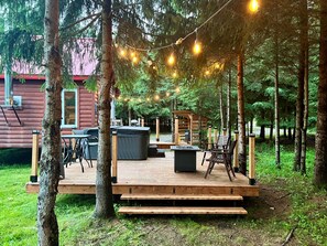 A wooden deck with outdoor furniture, string lights, and a view of a cabin in the background.