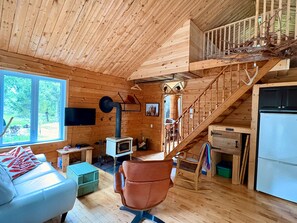 A wooden cabin interior with a sofa, a chair, a television, a fireplace, and a staircase.