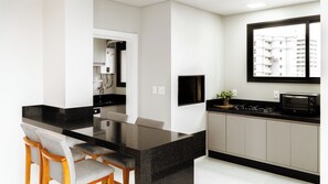 A modern kitchen with a black countertop, a built-in microwave, and a window overlooking a residential area. - 30m from the beach • 2 Suites • Grill • Garage (Porto Belo)