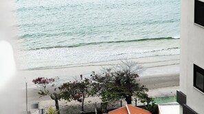 Blick auf einen Strand mit Wellen, sandigem Ufer und Bäumen.