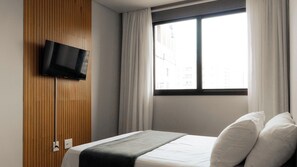 Hotellihuone, jossa on sänky, puupaneeliin asennettu televisio ja ikkuna, jossa on verhot.