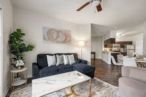 A modern living room with a dark grey sofa, a marble coffee table, and a large abstract painting on the wall. - Charming 2-bedroom apartment with AC in Dallas (Dallas)