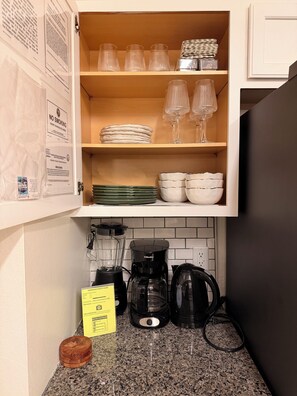 A kitchen with a wooden cabinet containing glassware, plates, and a coffee maker. - Elegant Renovated Home with Private Fenced Pool and 4 Spacious bedrooms (Davenport)
