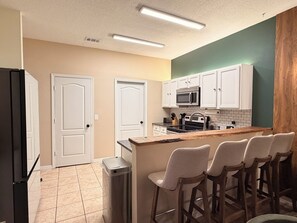 A kitchen with white cabinets, a stainless steel refrigerator, a microwave, and a wooden island with bar stools. - Elegant Renovated Home with Private Fenced Pool and 4 Spacious bedrooms (Davenport)