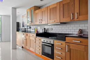 A modern kitchen with wooden cabinets, a black stove, and white tiled backsplash. - 4 bedroom & bathroom pool villa, with golf view. Only 7km to Patong (Tambon Kathu)