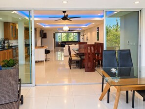 A modern interior with a dining area, kitchen, and sliding glass doors leading to a balcony. - 4 bedroom & bathroom pool villa, with golf view. Only 7km to Patong (Tambon Kathu)
