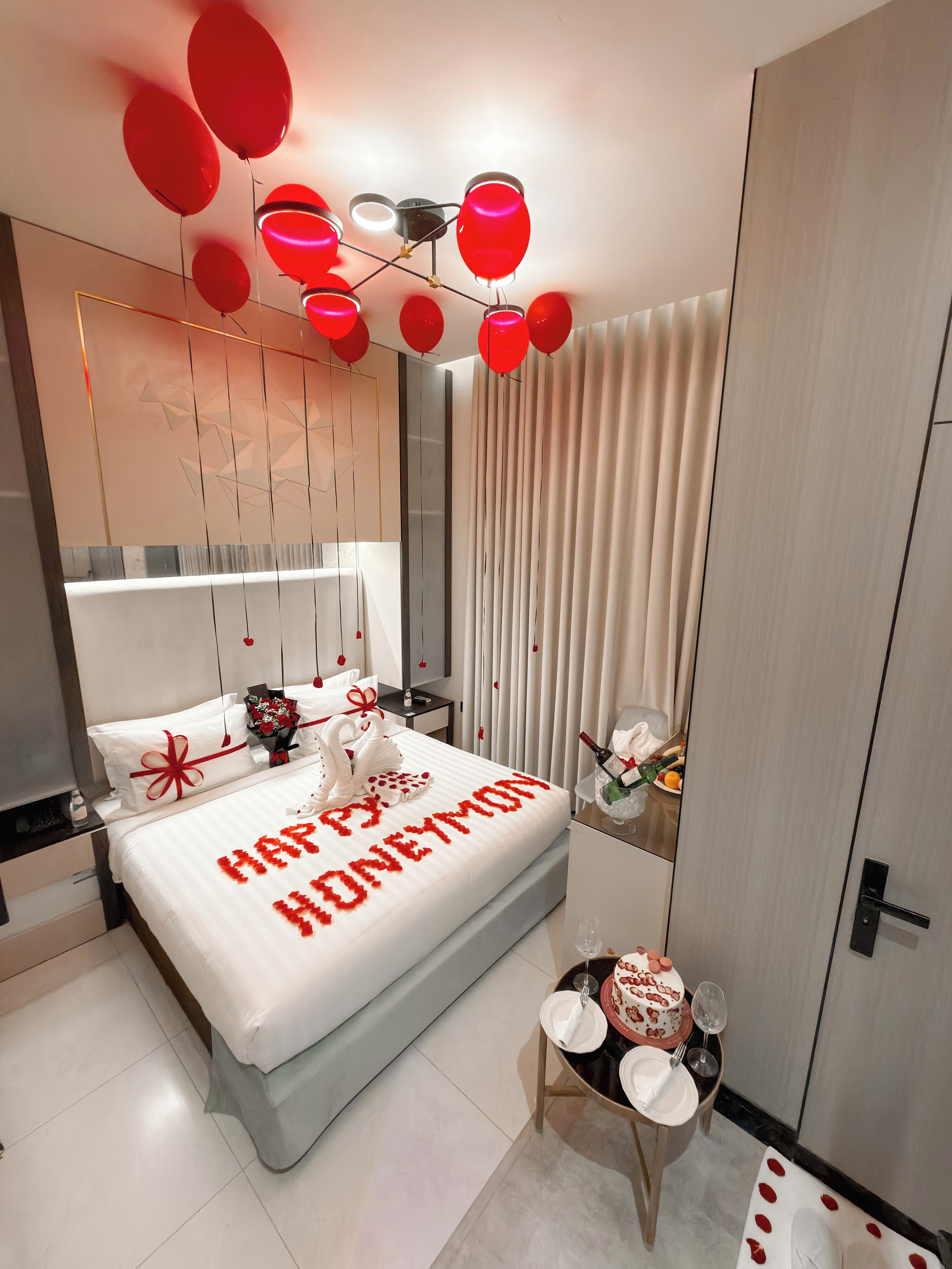A modern bedroom with a bed, a bedside table, a small table with a cake, and a wall-mounted light fixture.