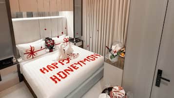 A modern bedroom with a bed, a bedside table, a small table with a cake, and a wall-mounted light fixture.