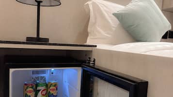 Ein Minikühlschrank mit Getränken, eine Lampe und ein Bett mit Kissen.