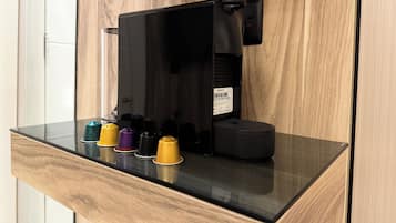 A coffee machine with a black body and a digital display, placed on a black countertop with a wooden panel background.