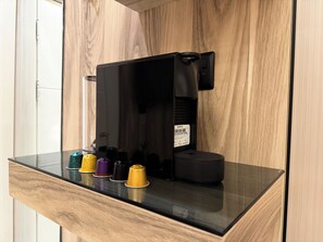 A coffee machine with a black body and a digital display, placed on a black countertop with a wooden panel background. - Mayyoun  serviced apartments (Riyadh)