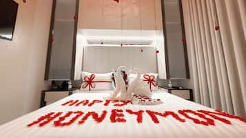 A hotel room with a bed adorned with rose petals spelling 'HONEYMOON' and two swan-shaped pillows.