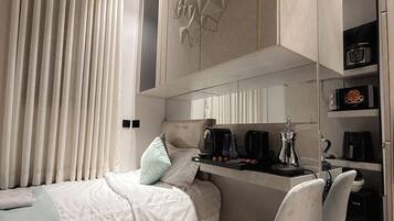 A modern bedroom with a bed, a desk, and a chair. There is a coffee machine and a microwave on the desk.